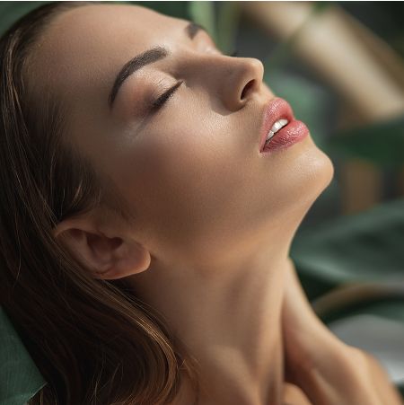 med spa patient model with closed eyes amidst green foliage.