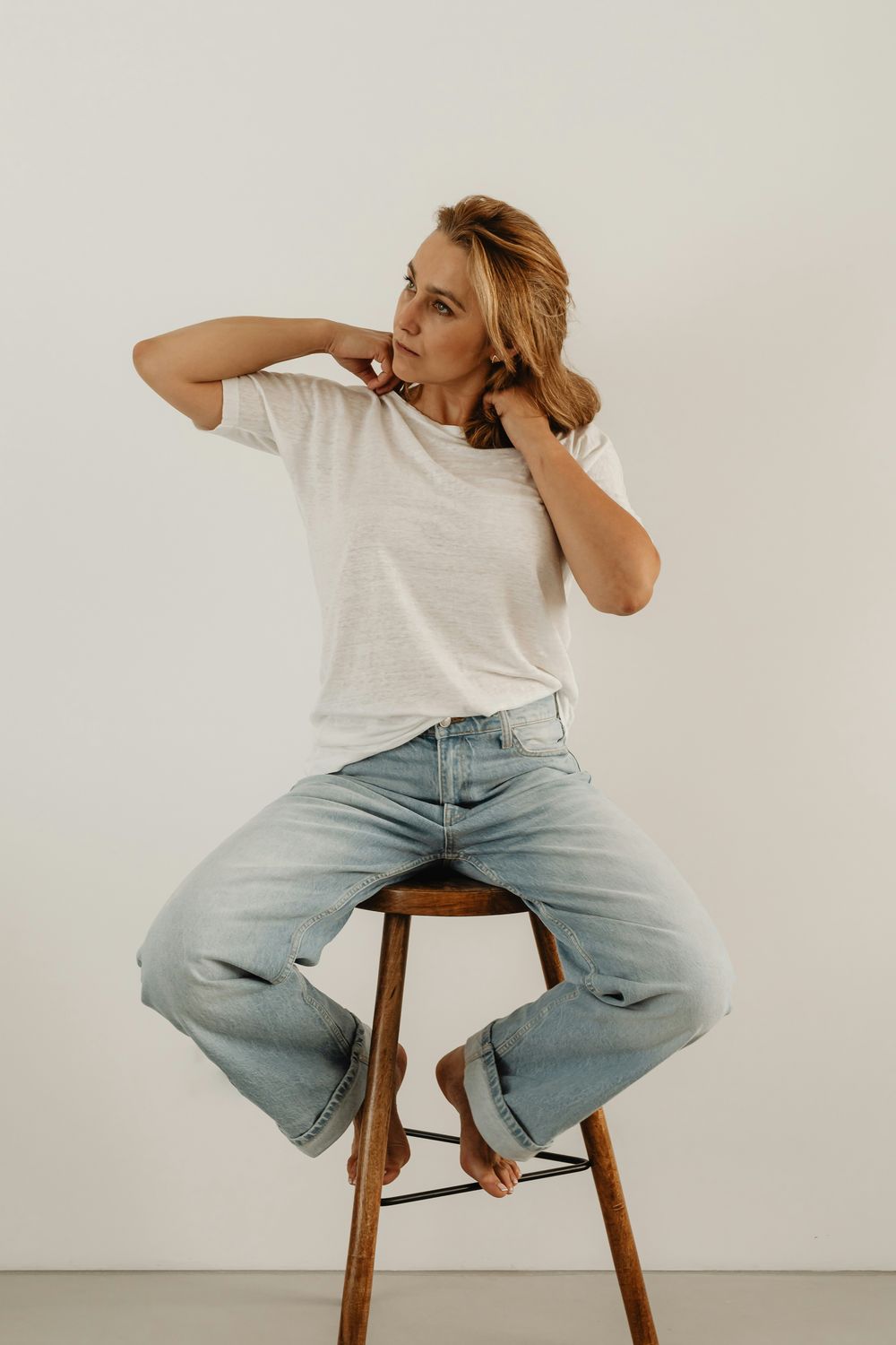 Woman sitting on stool, adjusting her hair.