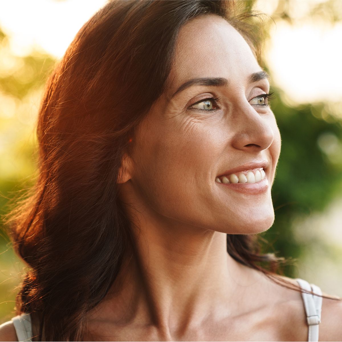 Smiling microneedling patient model in natural outdoor setting.