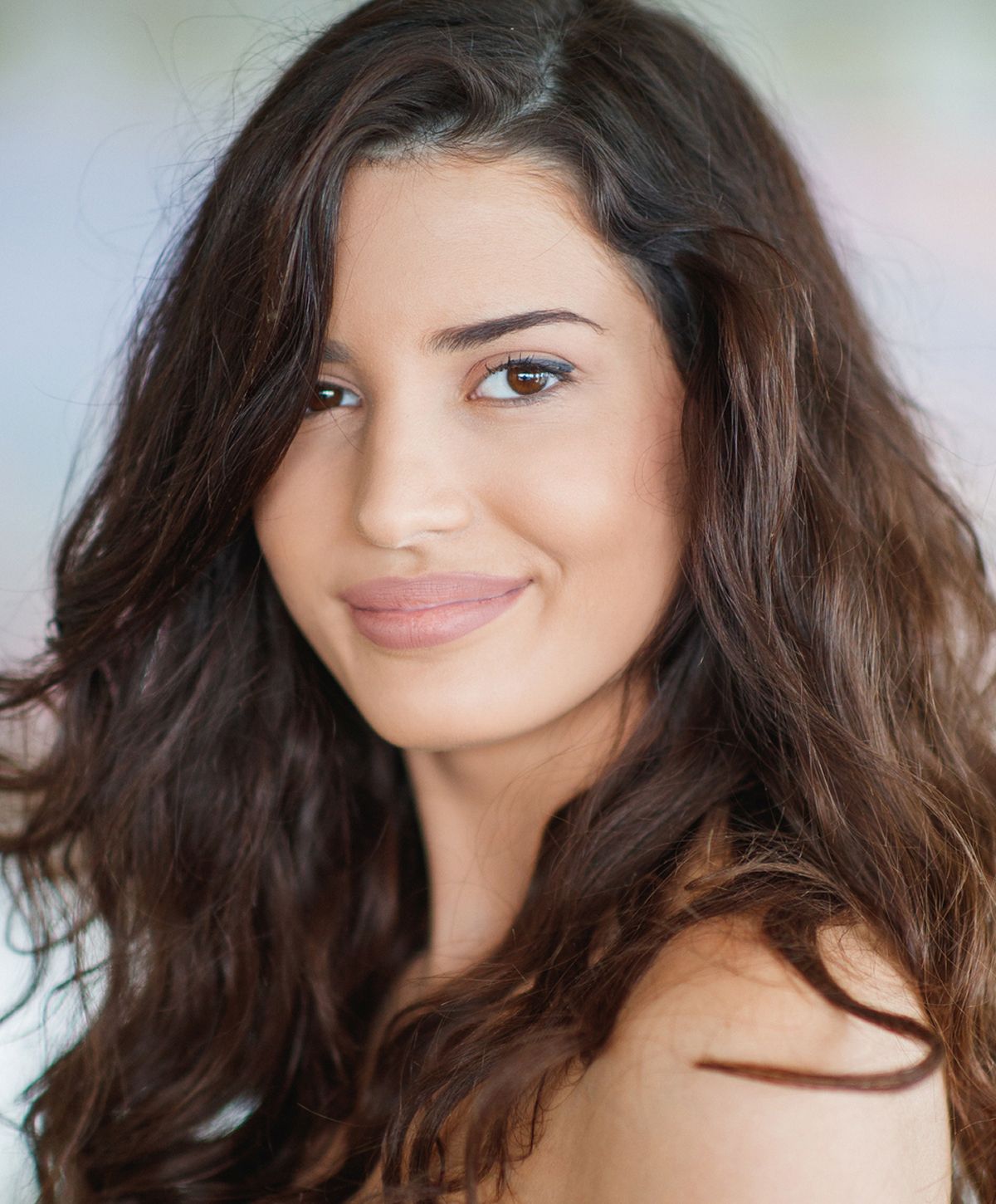 Smiling acne treatment patient model with long, wavy brown hair.