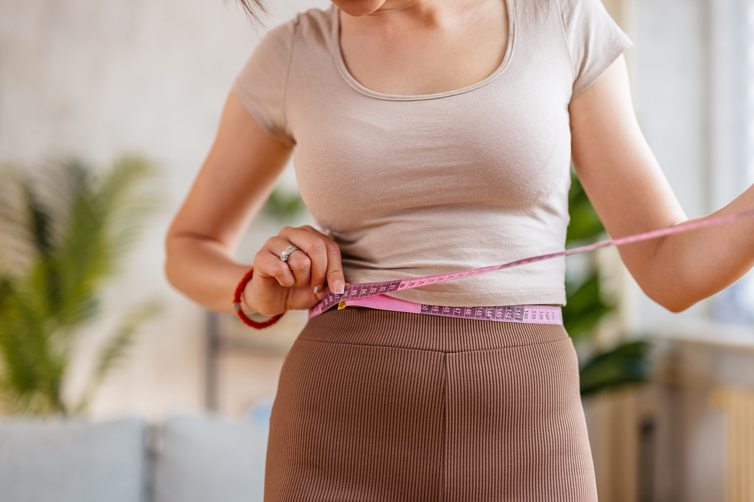 retratrutide patient model measuring her waist with a tape measure indoors.
