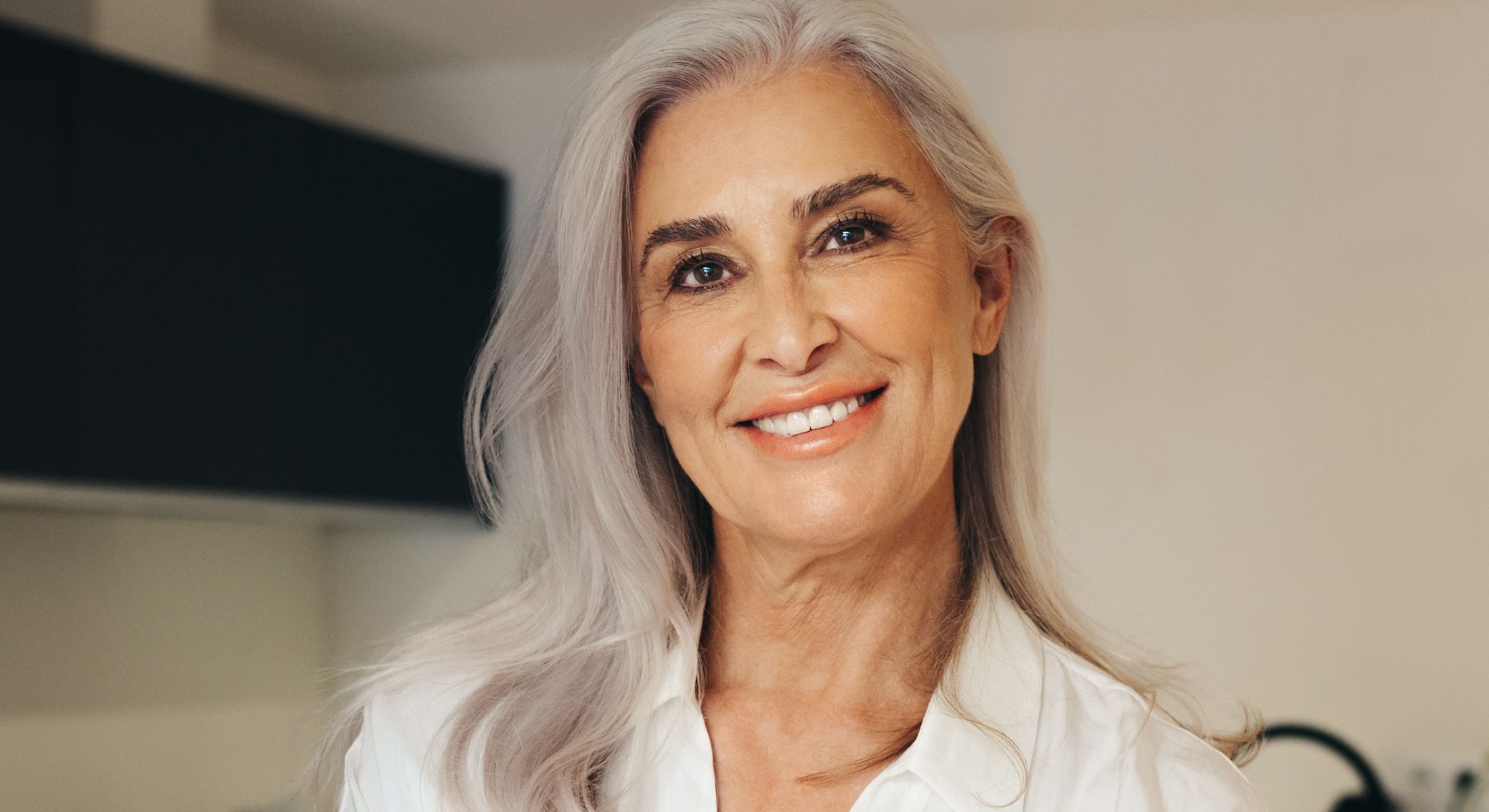Smiling older med spa patient model with silver hair in white blouse.