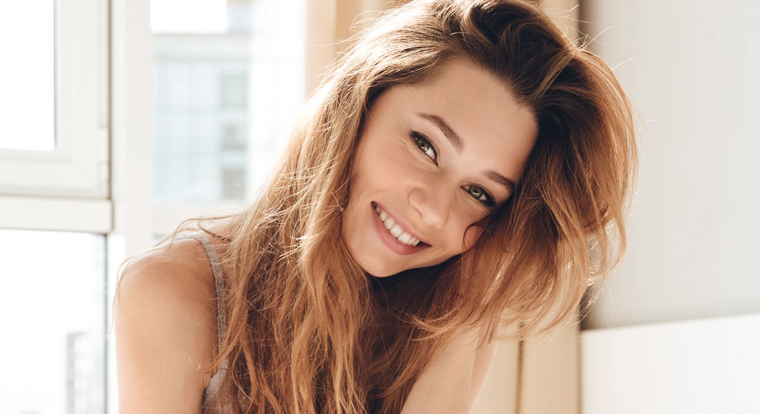 Smiling brow and lash services patient model with long hair in bright setting.